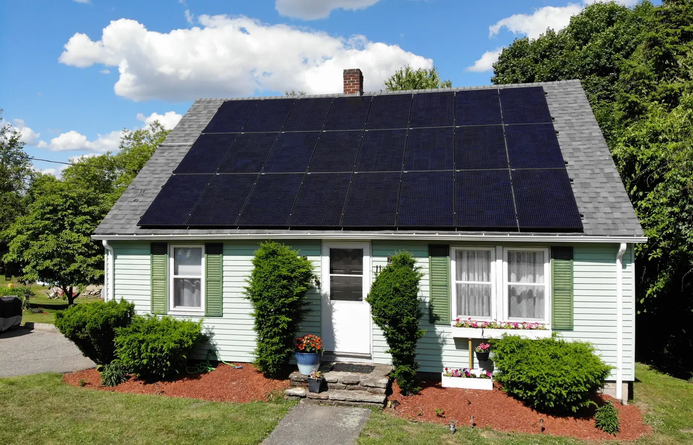 Green cape-style house with a full array of black solar panels