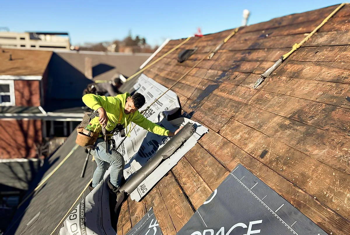Roofer installing underlayment on a stripped Massachusetts roof deck